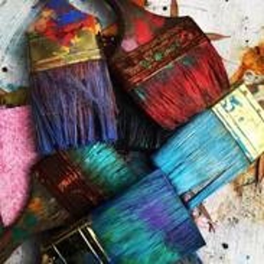 Mehrere Pinsel mit bunten Farbresten liegen auf einer Oberfläche